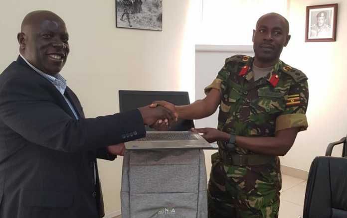 NITA-U’s James Saaka hands over one of the laptops to Col. Ahimbisibwe